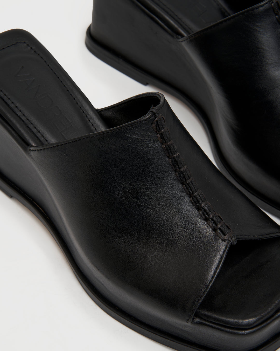 Women's wedge platform mule slide-on shoes made from buttery soft premium European black leather. The shoe design features a wholecut upper, meaning that it's been cut in one continuous piece. The toe and heel of the shoe are a chiseled square shape. The insole is fully padded for all-day comfort and the nubuck sole features non-slip rubber inserts. The perfect 90s inspired cool girl shoe for spring summer and fall.