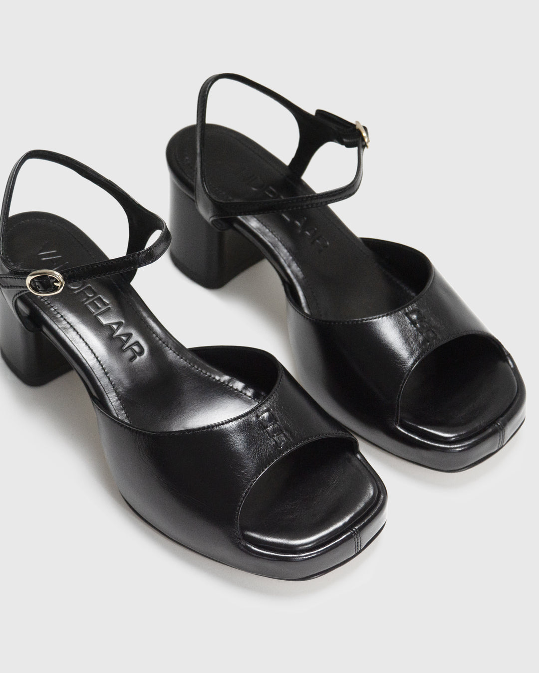 Women's mid-heel block heel open toe sandal with a concealed hidden platform of 2cm (3/4 inch) height and a stacked effect sturdy block heel of 6.5cm (2 3/4 inch) height. The elegant, minimal and timeless sandals comes with a dainty ankle strap that is elasticated to provide additional comfort. The insole is cut to a square toe shape and is fully padded for ultimate all-day comfort. This is the perfect 90's inspired cool girl sandal to wear all spring summer! Made from premium shiny black leather.